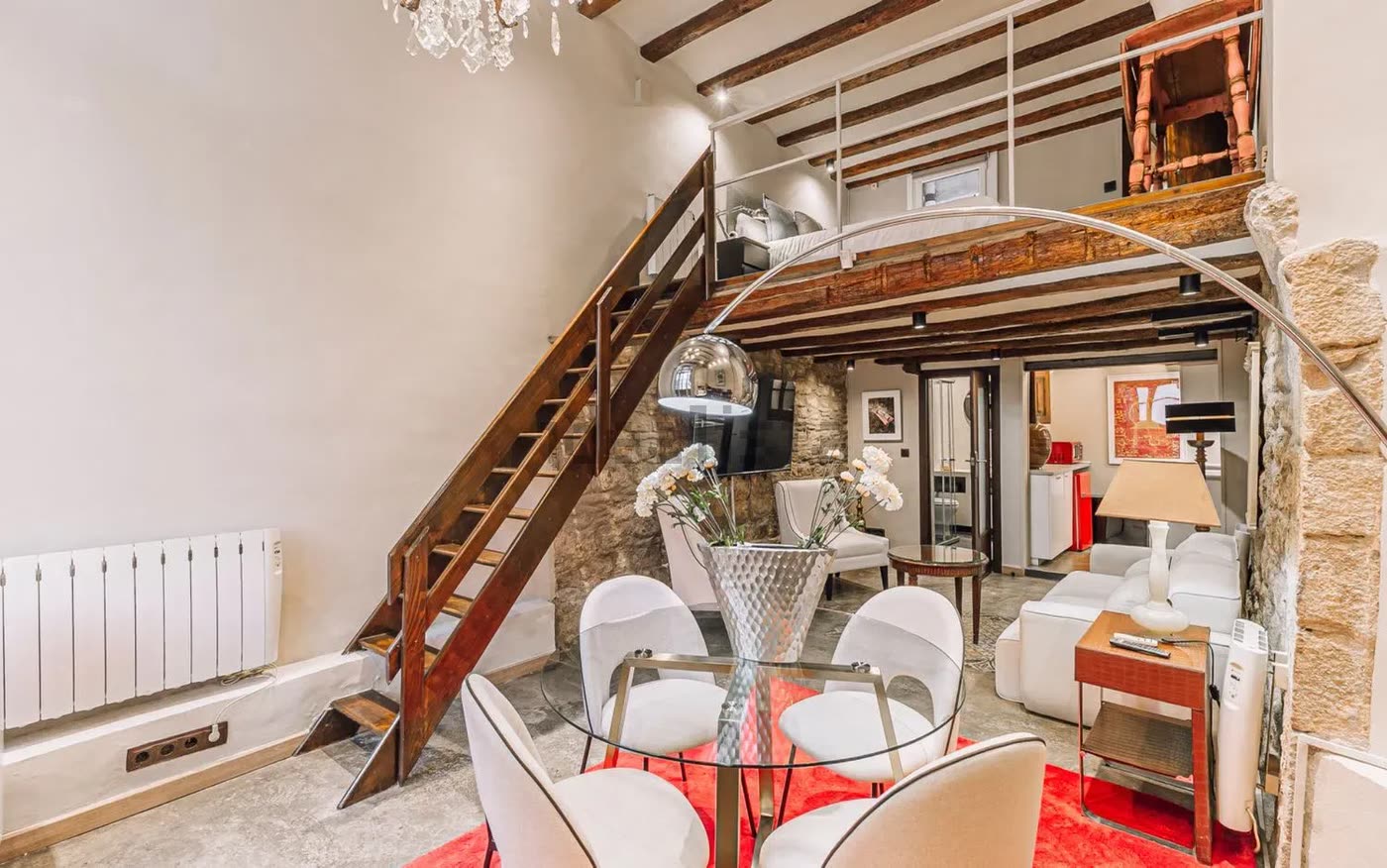 Escalera de madera al altillo junto a la mesa de comedor de cristal