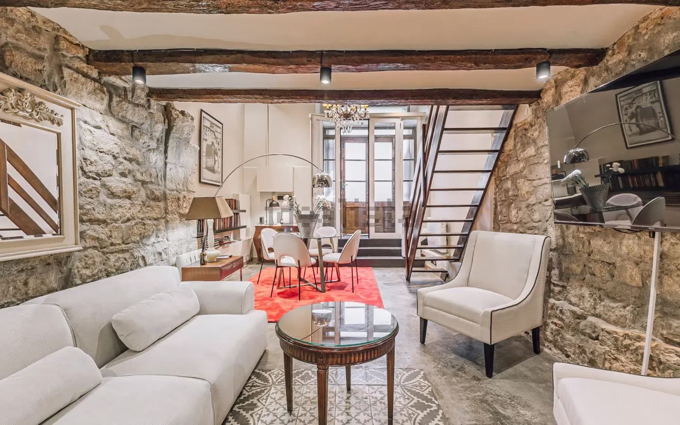 Salón del loft de El Born, con paredes de piedra vista, vigas de madera y la escalera al altillo