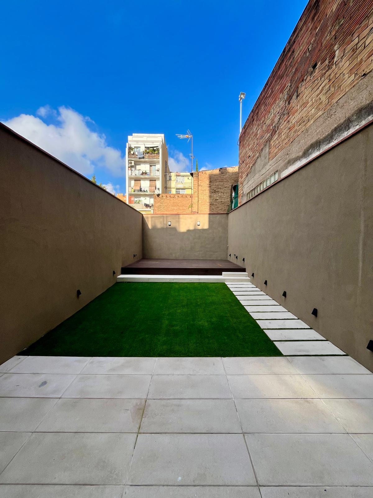 Jardín entre muros con el cielo abierto y la tarima de madera al fondo