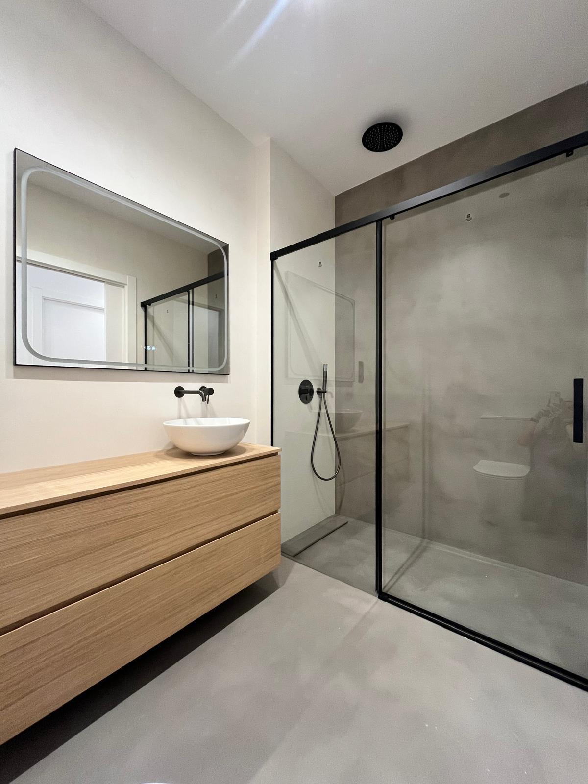Baño con ducha de obra, mampara negra y mueble de roble con lavabo sobre encimera